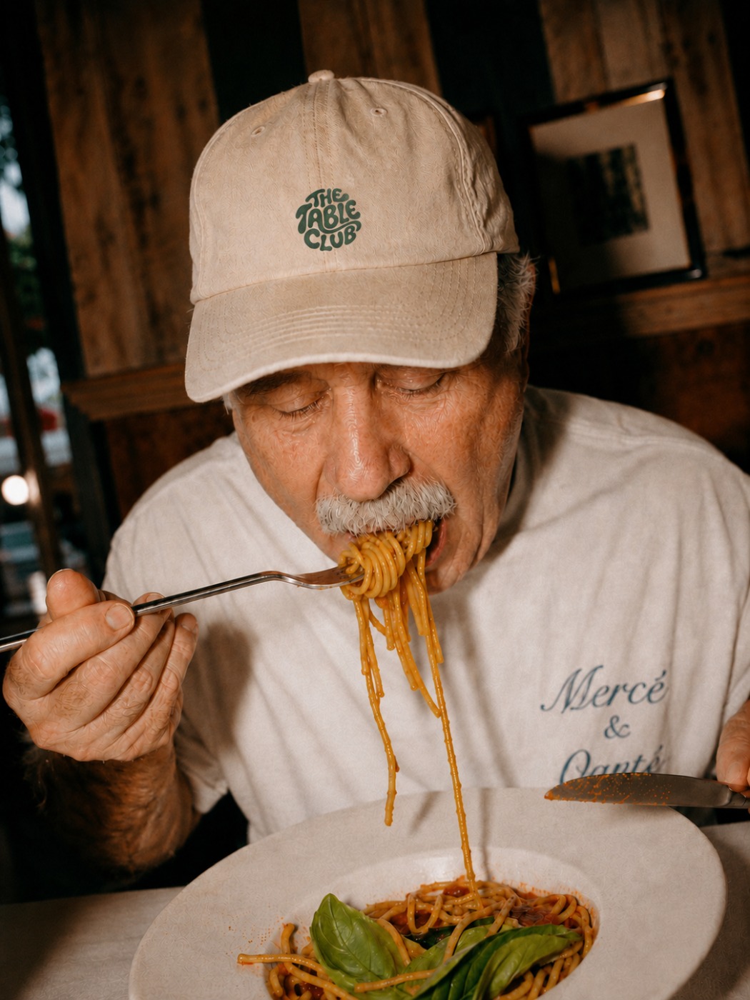 A Table Club regular wearing the branded cap, twirling pasta at the table