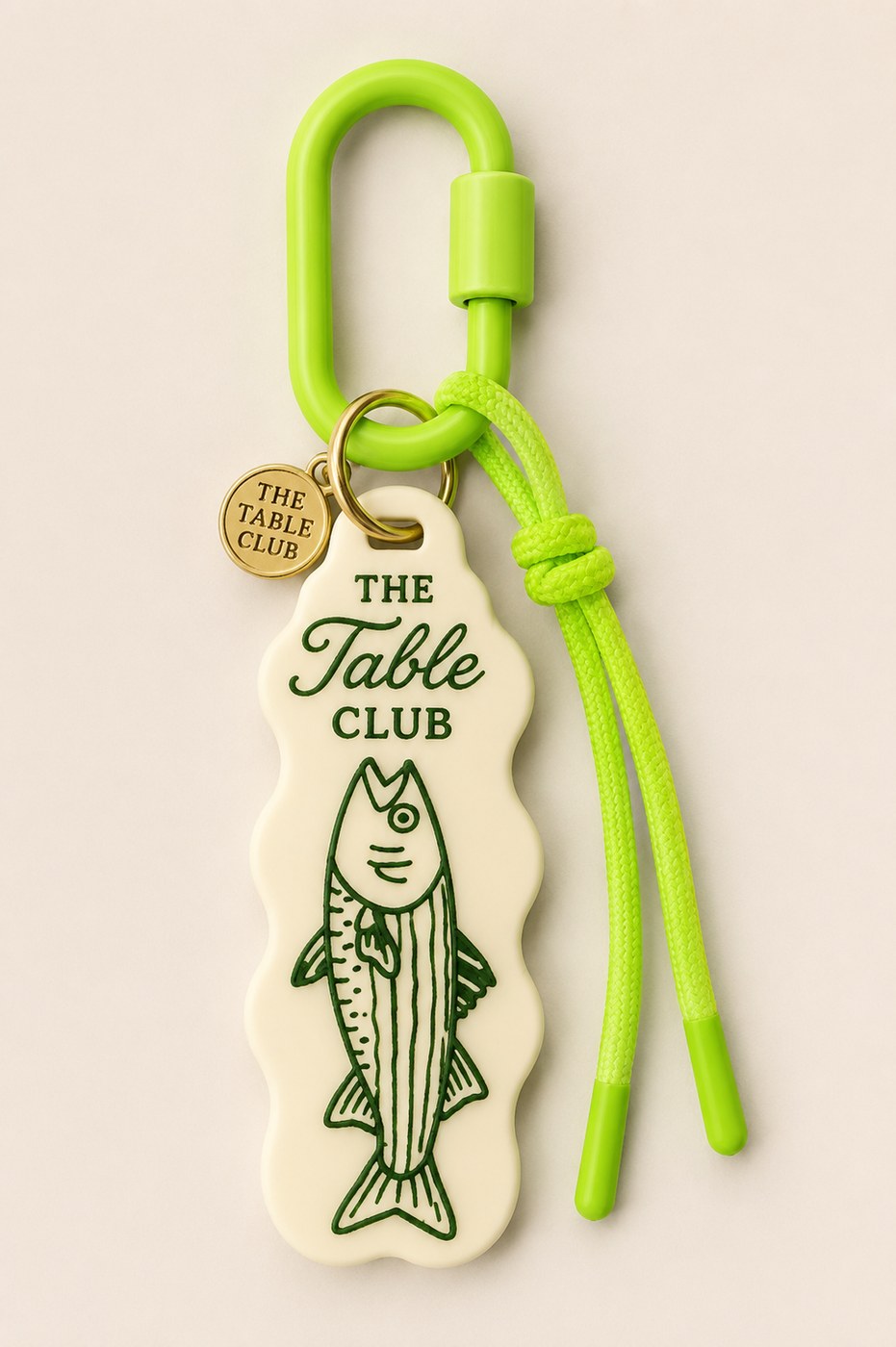 A lime-green Table Club keychain with a hand-drawn fish charm